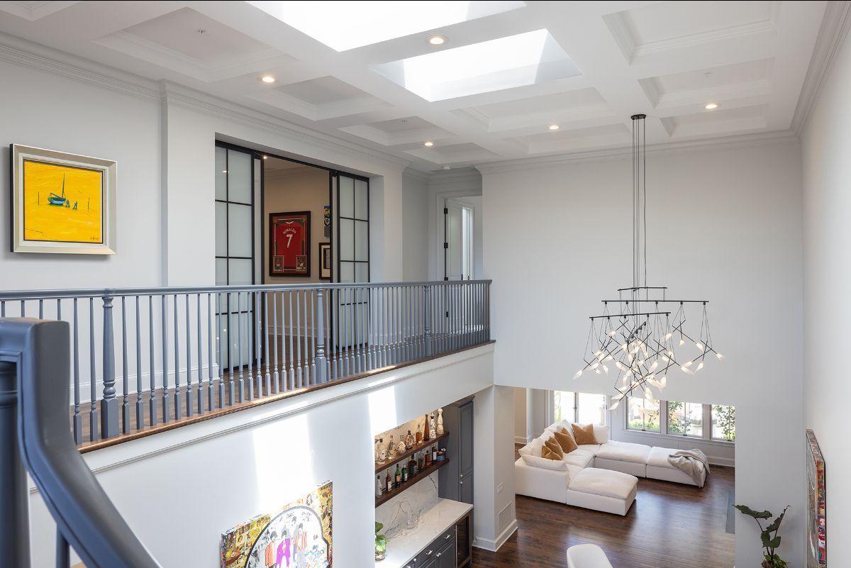 An elevated view of a modern two-story home interior, featuring a balcony railing, skylights, and a chandelier.