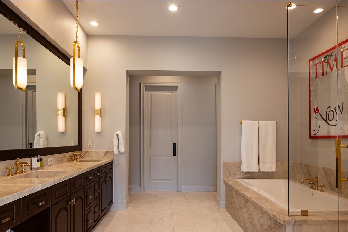 A luxurious bathroom with a dark vanity, double sinks, a soaking tub behind a glass partition, and a framed Time poster.