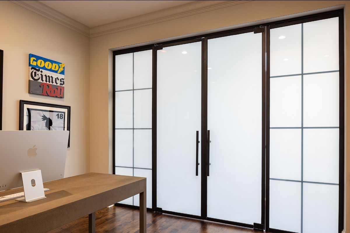 Modern home office featuring a wooden desk, computer, and large black-framed doors with frosted glass panels.