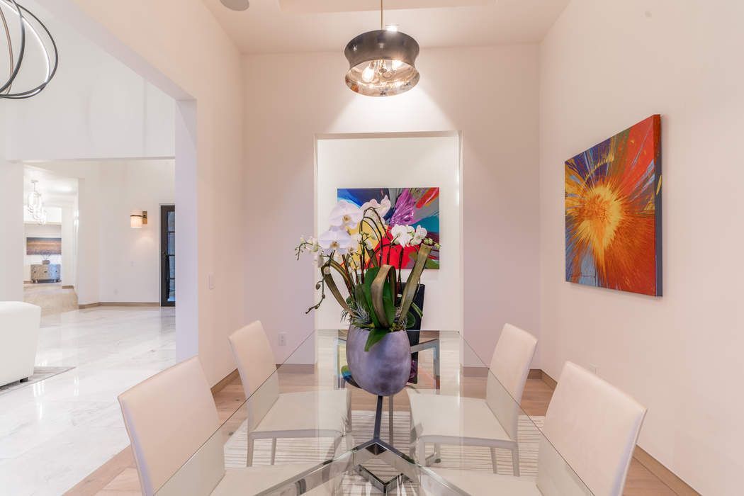 Dining area with a glass table, four modern chairs, a large floral centerpiece, and colorful abstract art on the walls.