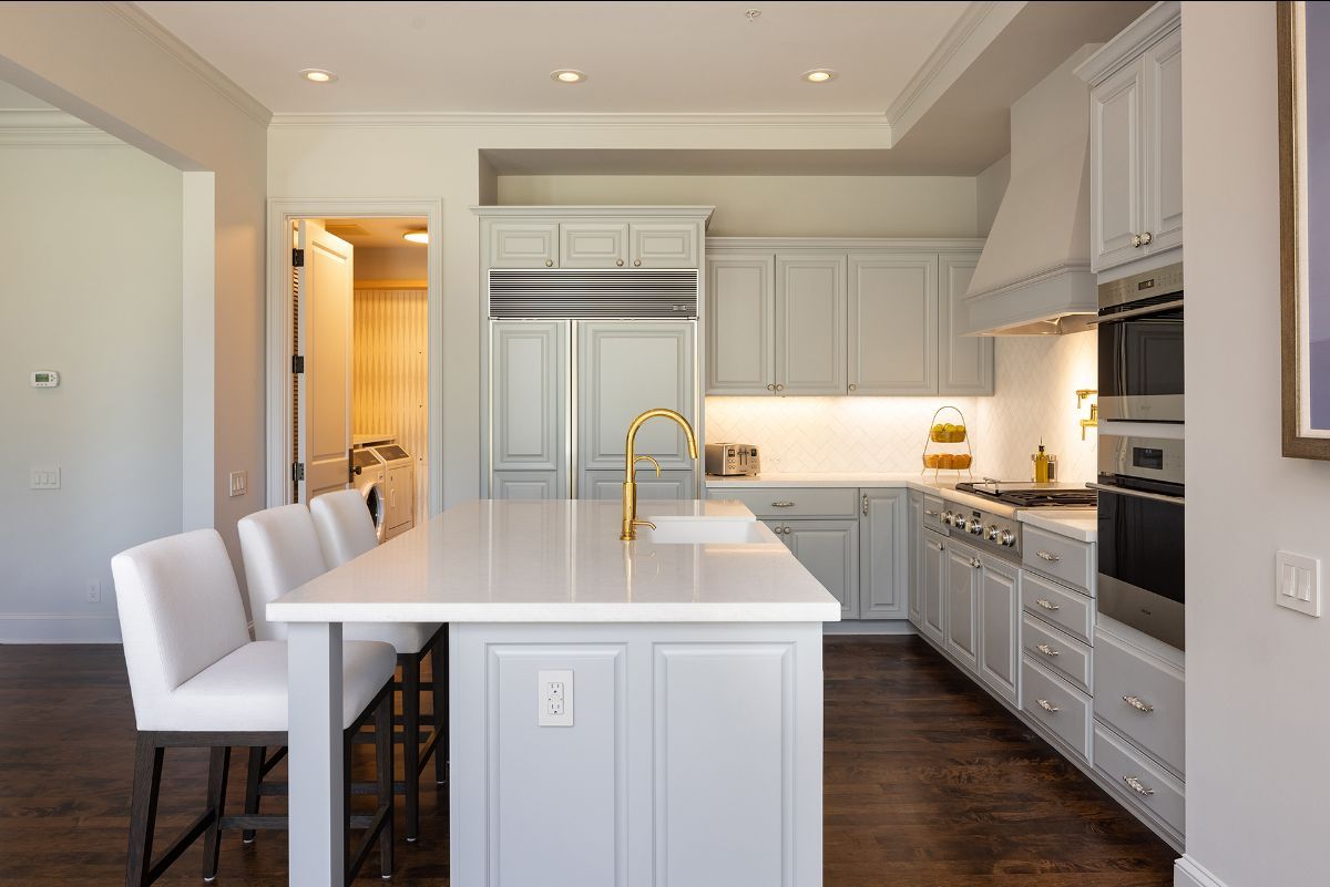 A bright, modern kitchen with a white quartz island, pale gray cabinetry, stainless steel appliances, and wood floors.