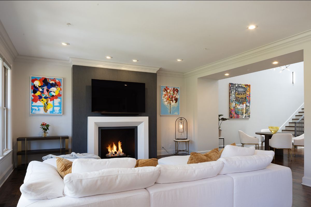 A modern living room with a large white sofa facing a dark accent wall featuring a television above a fireplace.