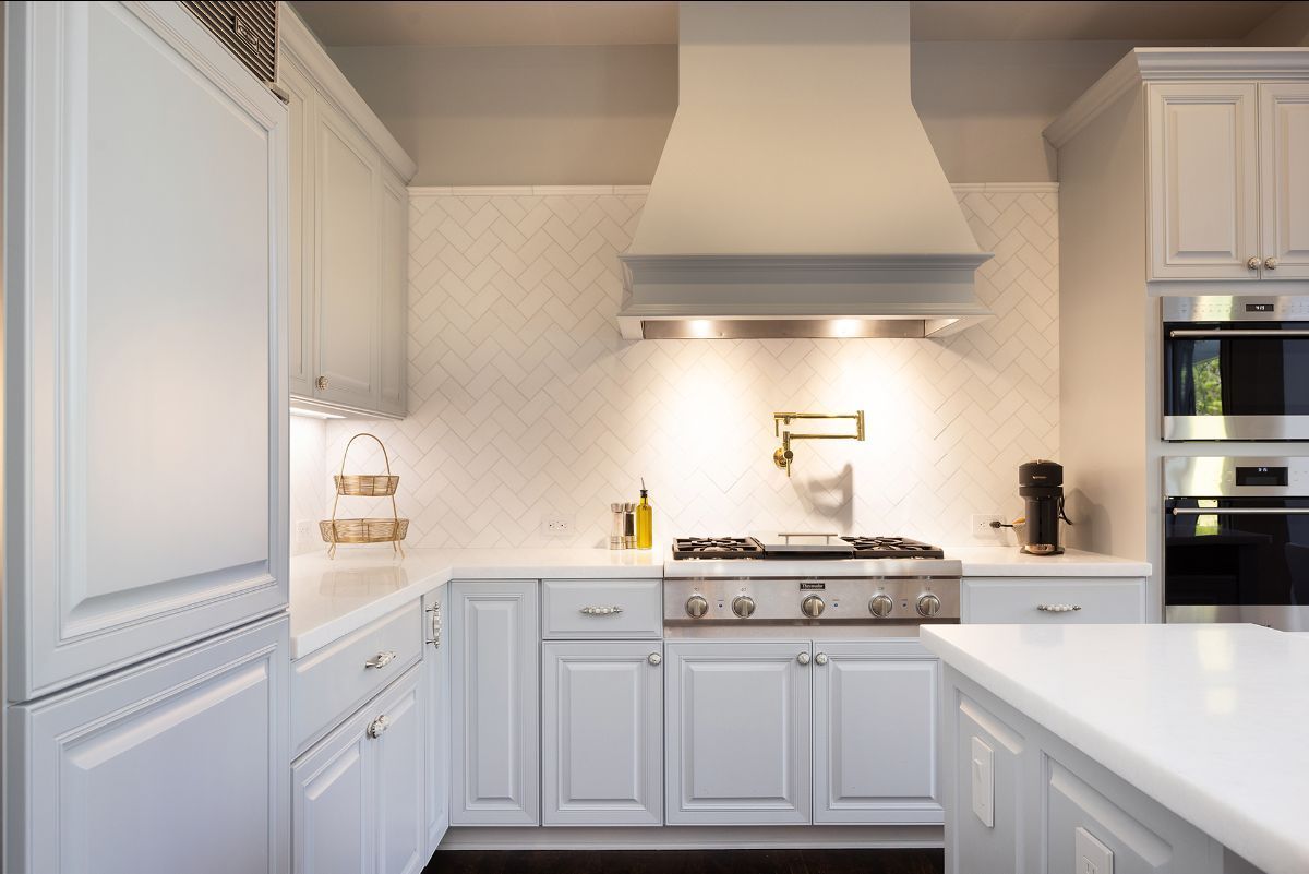 A bright, modern white kitchen featuring custom cabinetry, a herringbone tile backsplash, and a professional-style range.