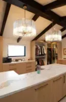 A spacious walk-in closet featuring light wood cabinetry, a marble-topped island, exposed dark beams.