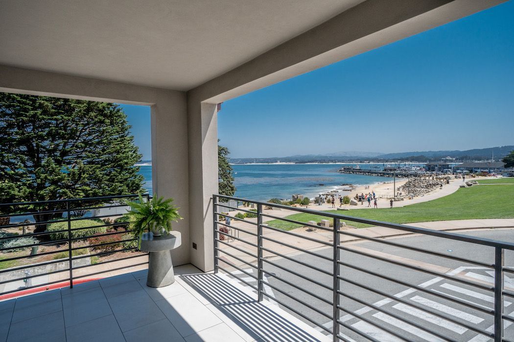 A covered balcony overlooking a sandy beach, park, and blue ocean under a clear sky.