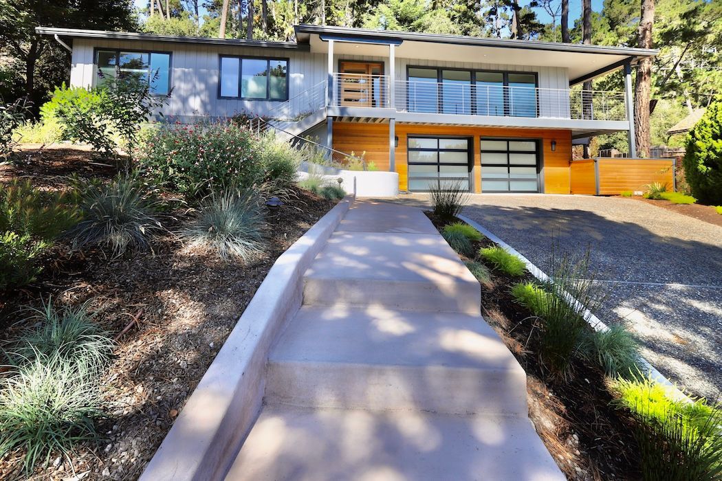 A mid-century modern house with a wood-paneled lower level, two-car garage, and concrete steps leading to the entrance.