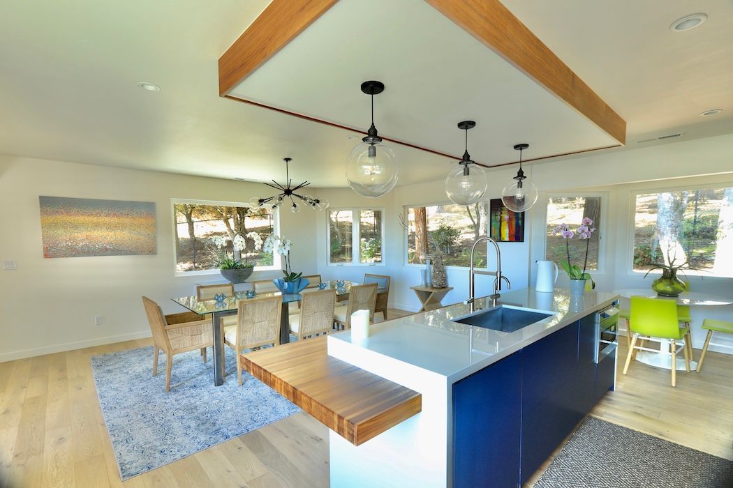 A bright, open-concept kitchen and dining area featuring a navy blue island, wooden ceiling accent, and light wood floors.