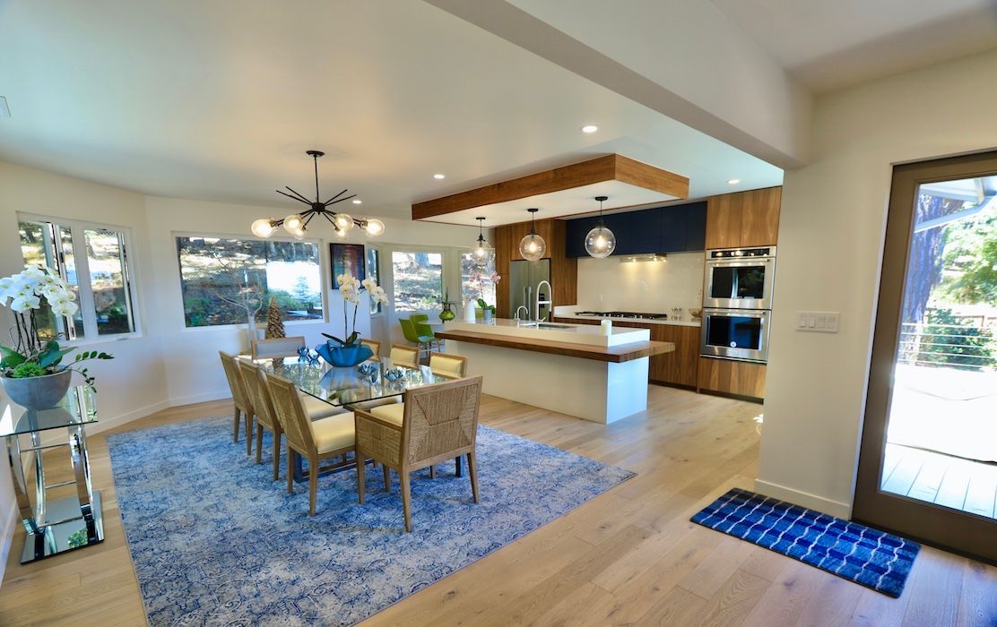 A spacious, modern open-plan dining and kitchen area with light wood floors, a blue rug, and wooden cabinetry.
