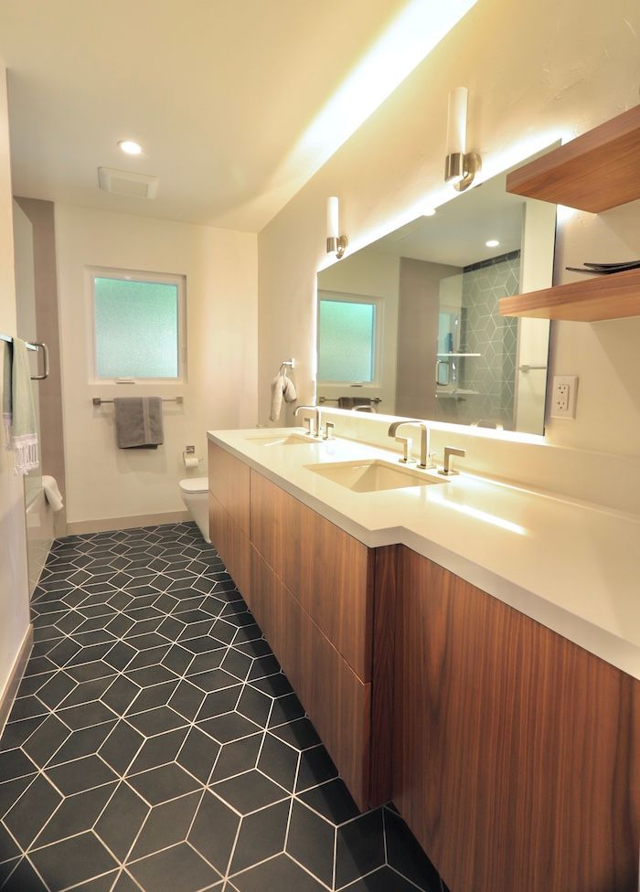 Modern bathroom with wood vanity, white countertop, geometric black-and-white tiled floor, and a large mirror.