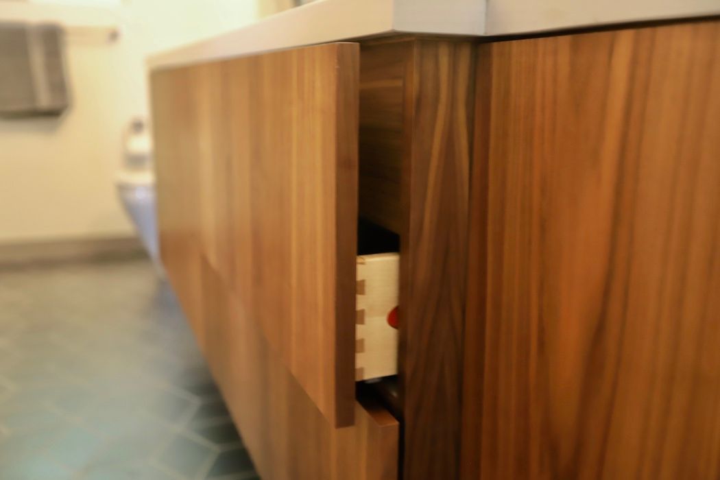 Close-up of a modern wood bathroom vanity with one drawer slightly open, showing light-colored drawer construction inside.