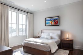 Modern bedroom with a wooden bed frame, white bedding, nightstands, floor-to-ceiling curtains, and framed wall art.