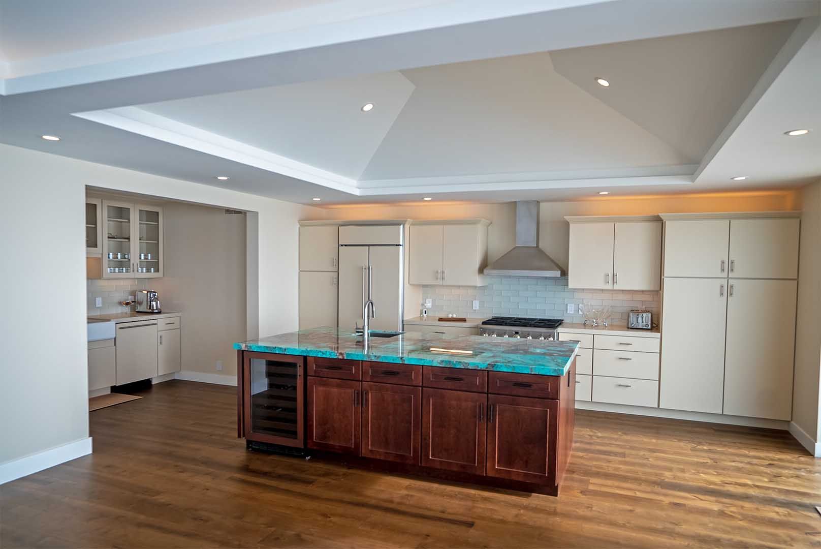 A kitchen with a dark wood island and turquoise countertop, light cabinets, and a vaulted ceiling in an open floor plan.