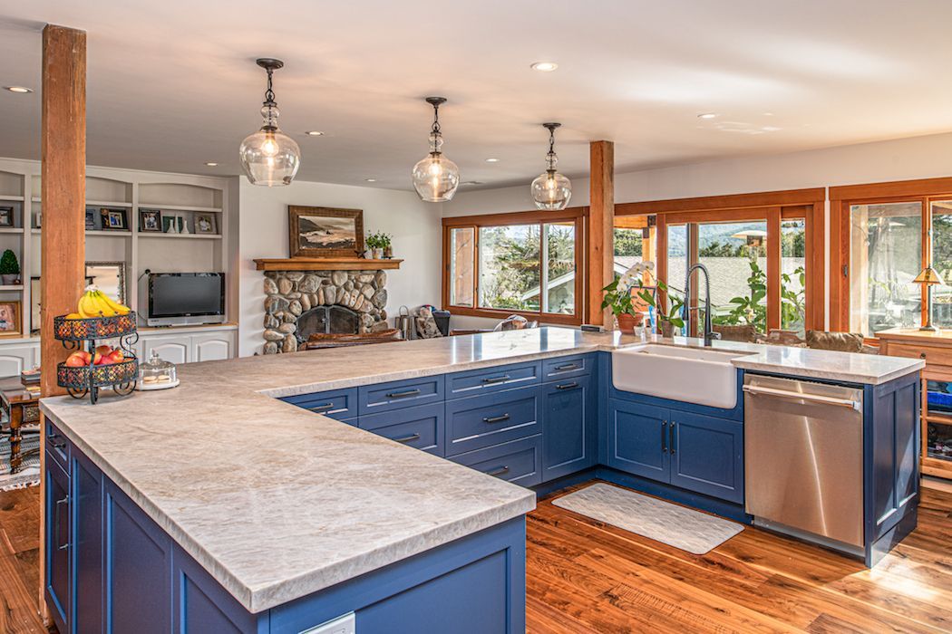 A blue U-shaped kitchen island and cabinetry with light stone countertops set against hardwood floors in an open room.