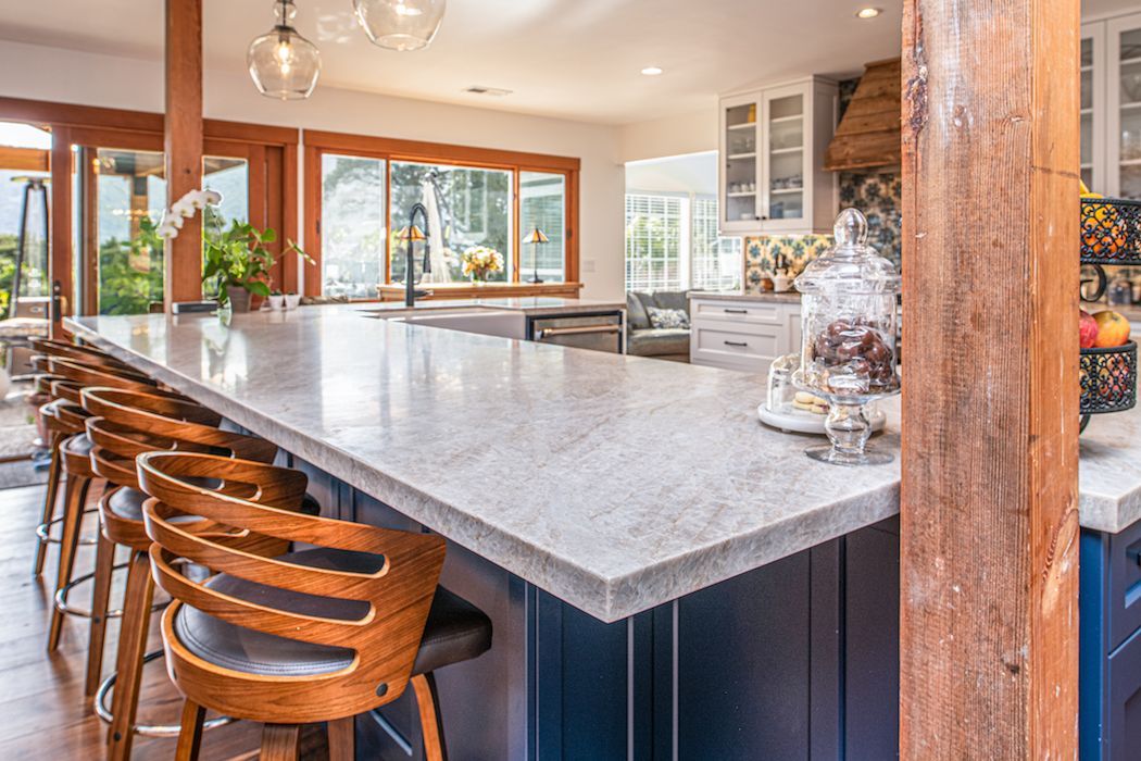 A modern kitchen island with a stone countertop and blue cabinetry, featuring wooden bar stools in a bright, open space.