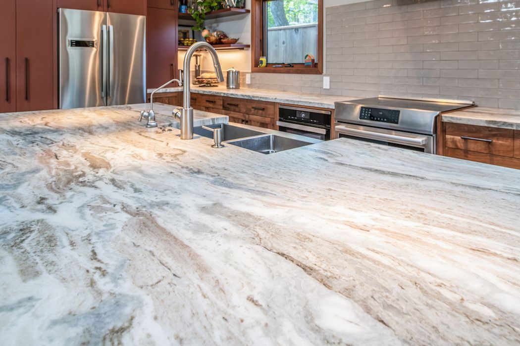 A high-angle shot of a kitchen featuring a large, swirling marble island countertop, a stainless steel sink, and stove.