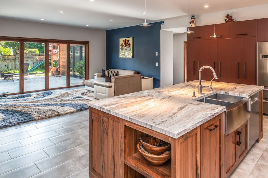 Modern kitchen with a wood island and marble countertop, opening into a bright living area with a blue wall and patio door.