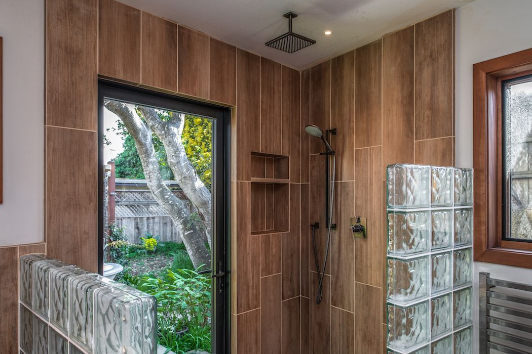 Shower area with wood-look tile walls, a glass block partition, a rainfall showerhead, and a door looking out to a garden.