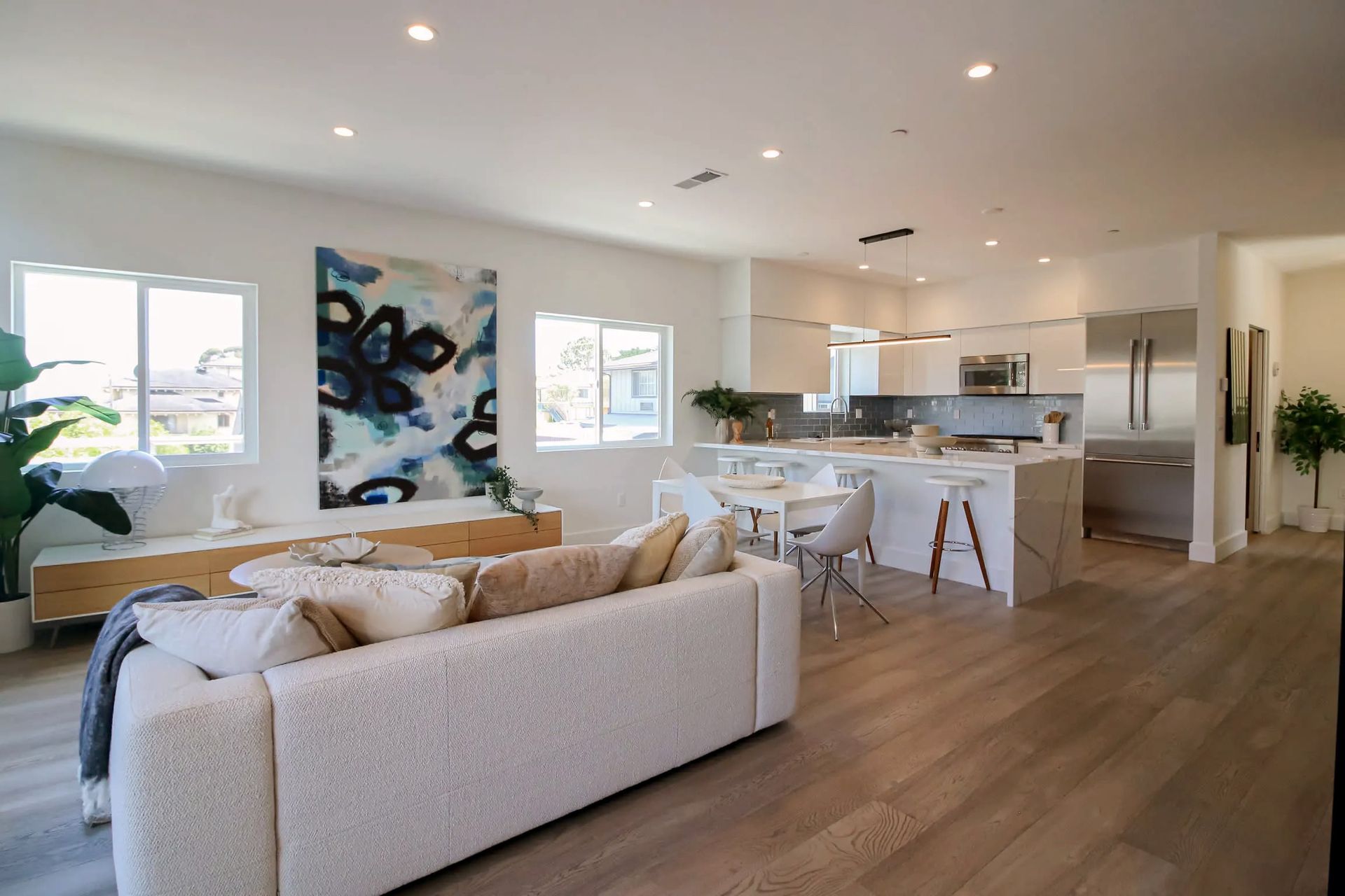 A spacious open-plan living room and kitchen with white walls, light wood floors, a textured sofa, and modern decor.