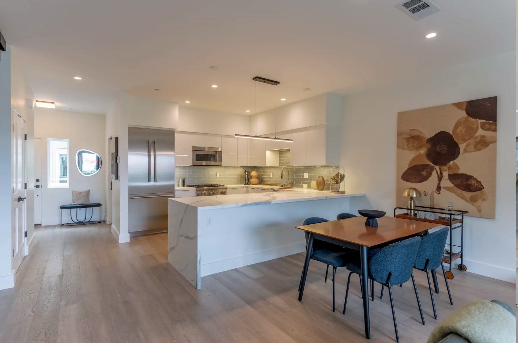 Modern, open-plan kitchen with white cabinets, a marble island, and a dining area with a wooden table and blue chairs.
