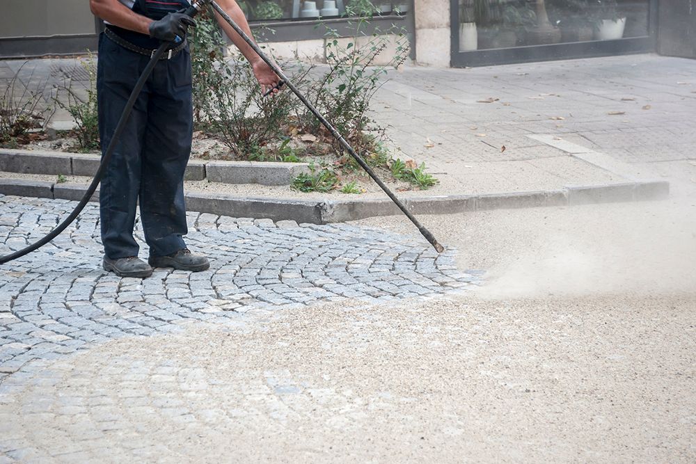 A man is using a high pressure washer to clean a cobblestone sidewalk.