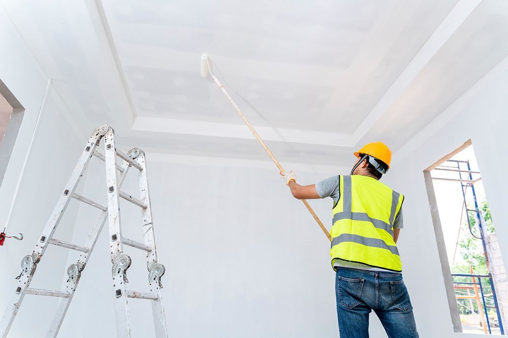 A man is painting the ceiling of a room with a roller.