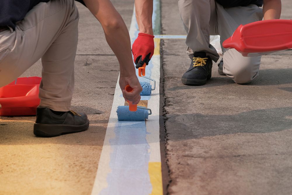 Two men are painting a line on the ground with paint rollers.