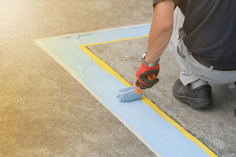 A man is kneeling down and painting a line on the ground with a roller.