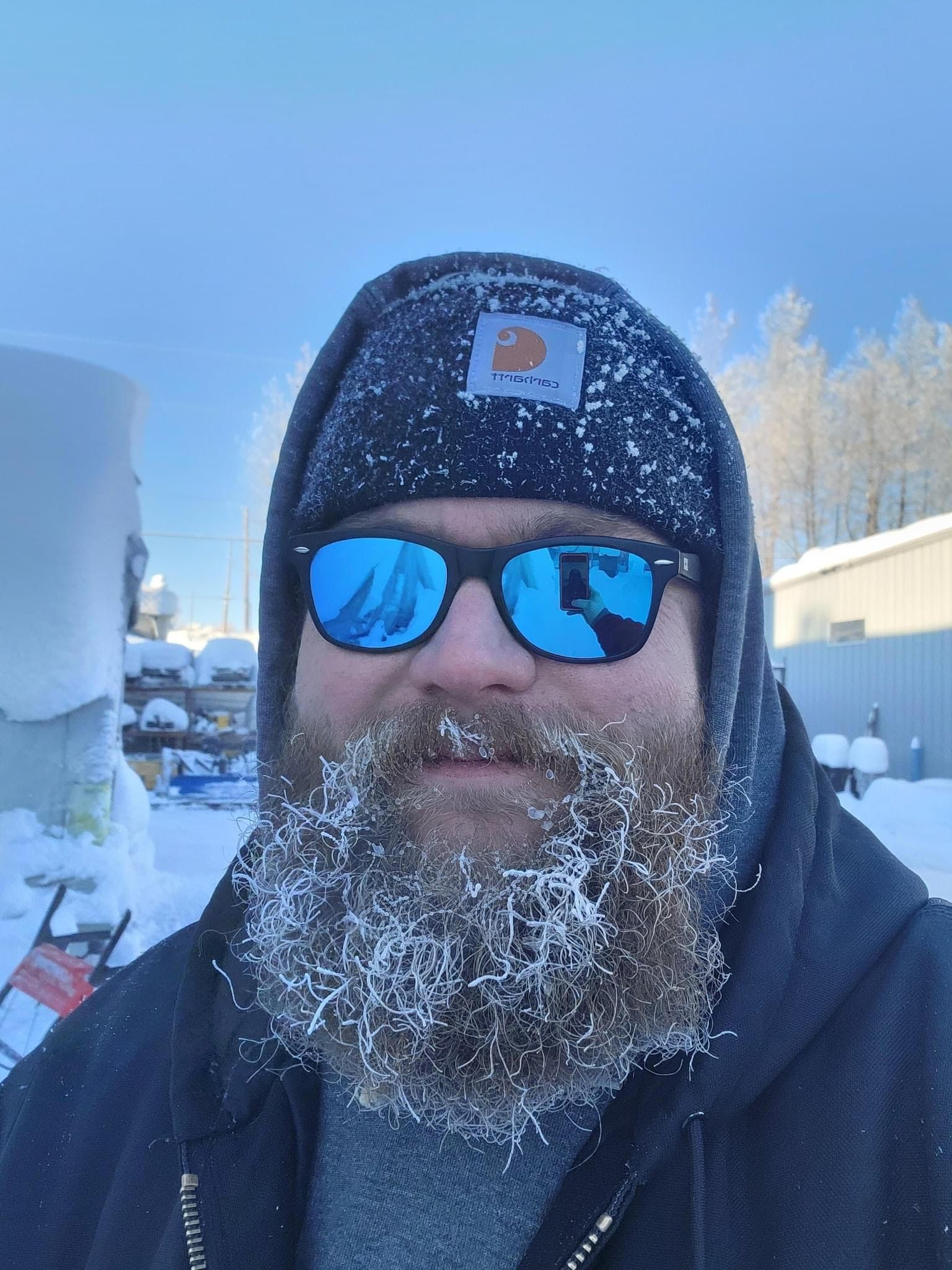 A man with a beard wearing sunglasses and a beanie is standing in the snow.