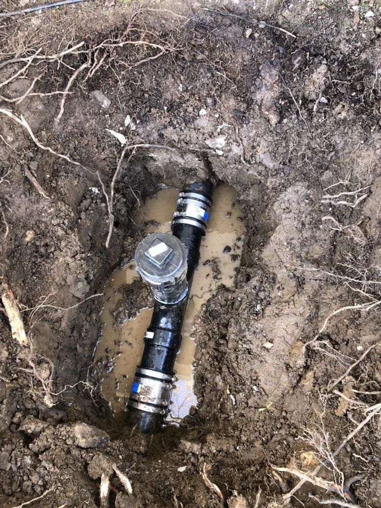 Black plumbing pipes in a muddy hole, possibly a repair.