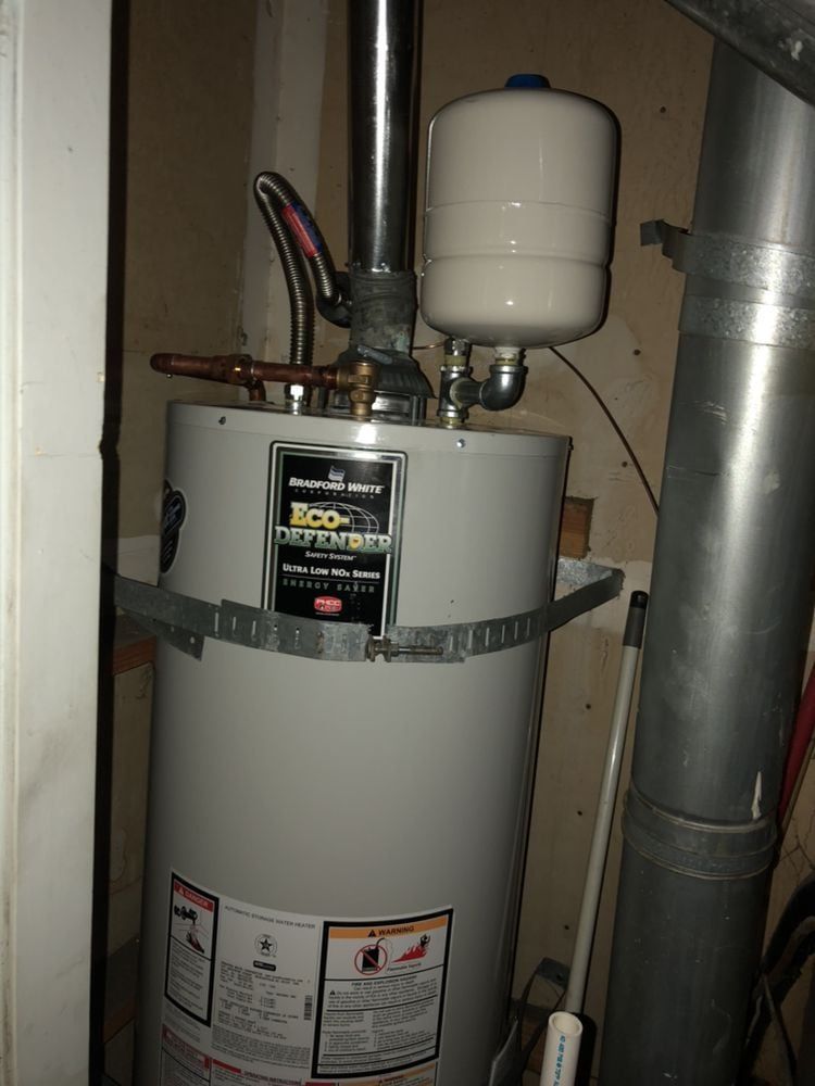 A water heater in a utility room, with an expansion tank on top and ductwork nearby.