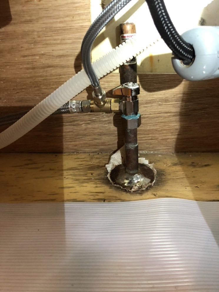 Copper pipe with shut-off valve and supply lines under a sink in a wooden cabinet.