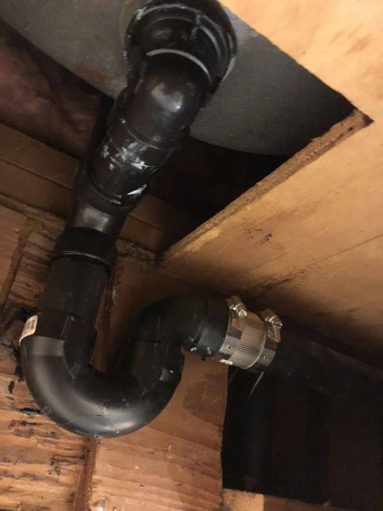Black plumbing pipes with a curved trap, connecting to a drain, installed in a wood-framed space.