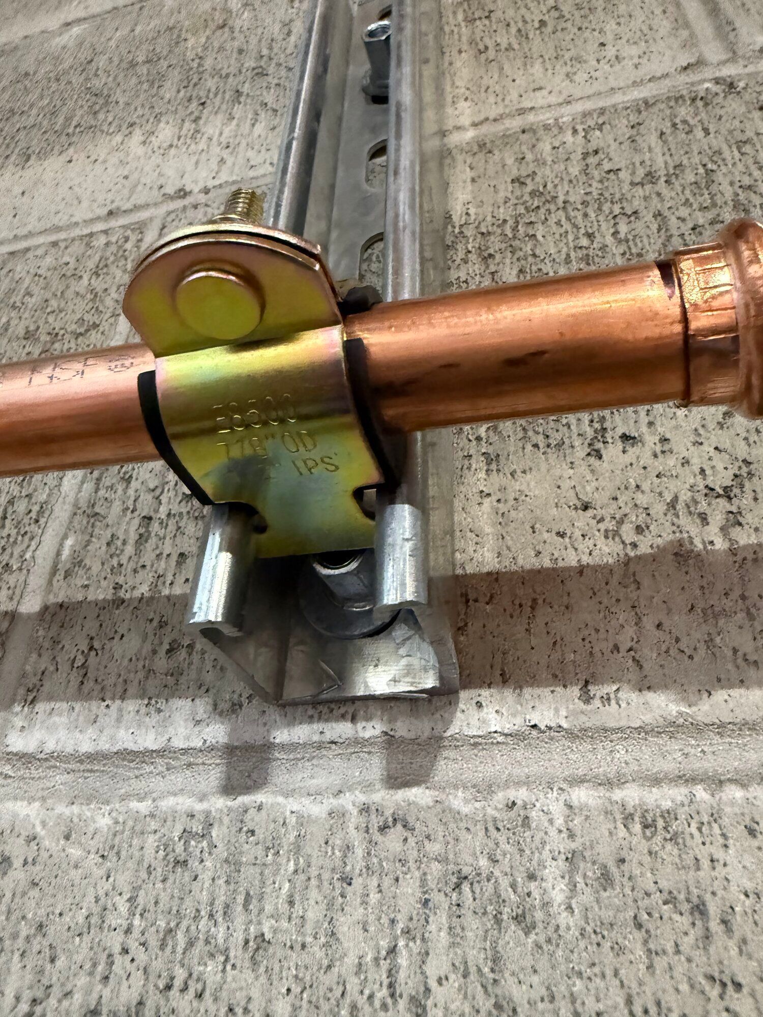 Copper pipe secured to a brick wall with a metal clamp and bracket.
