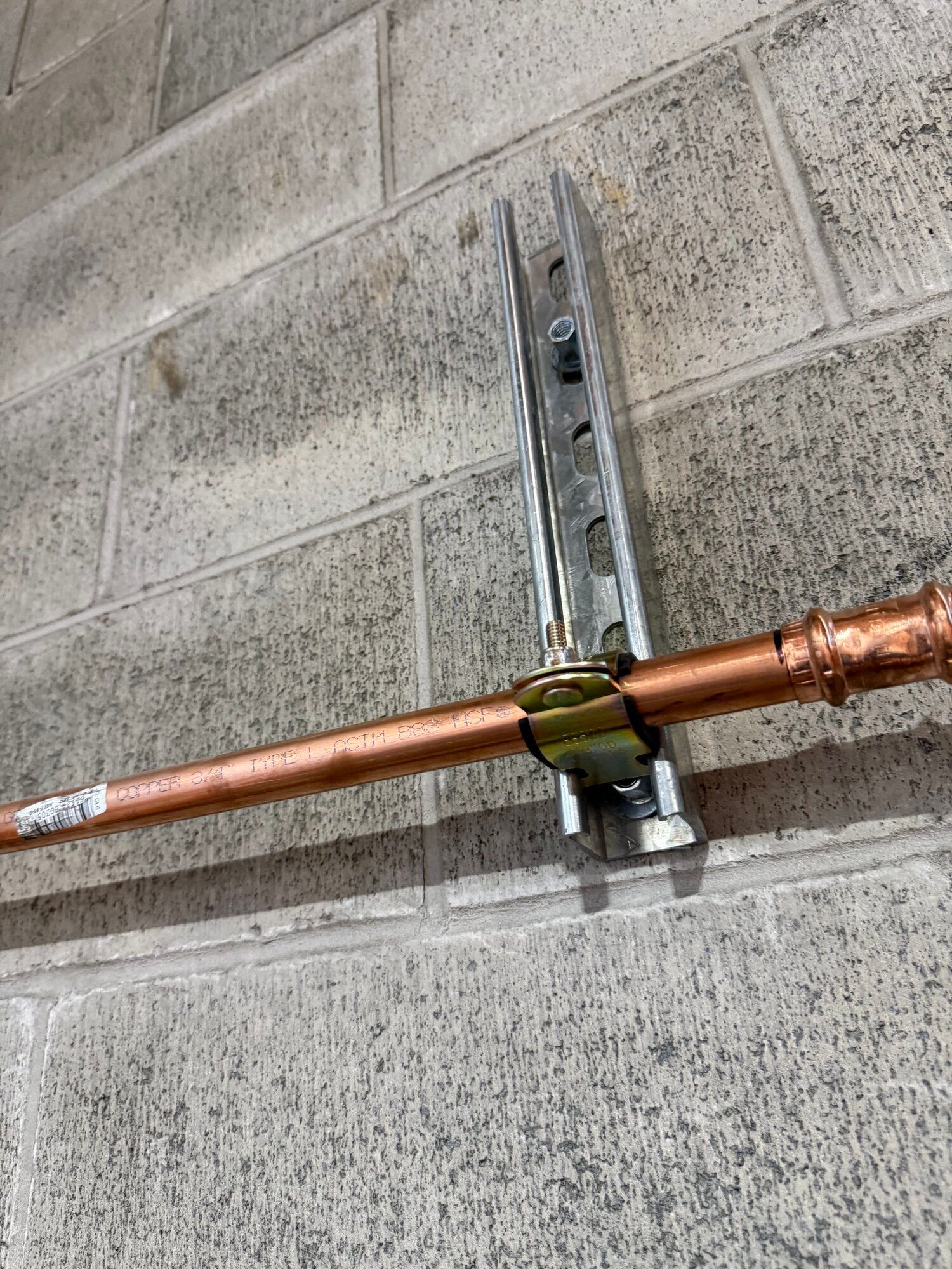 Copper pipe secured to a concrete block wall with a metal bracket and bolt.