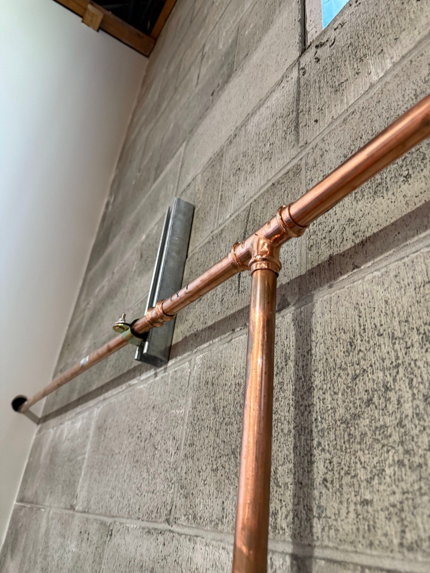 Copper plumbing pipes mounted on a gray cinder block wall, secured by a metal bracket.