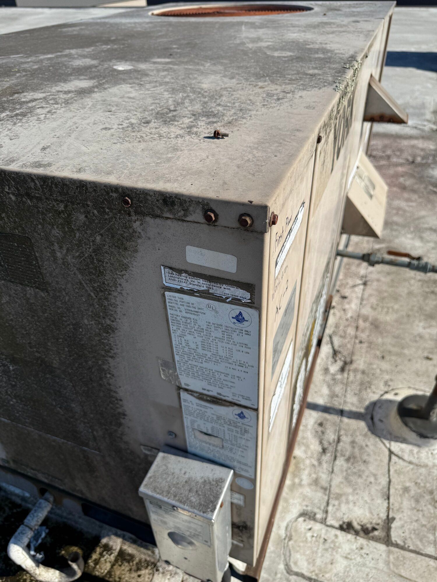 Rooftop air conditioning unit with weathered exterior and visible labels, mounted on a flat roof.