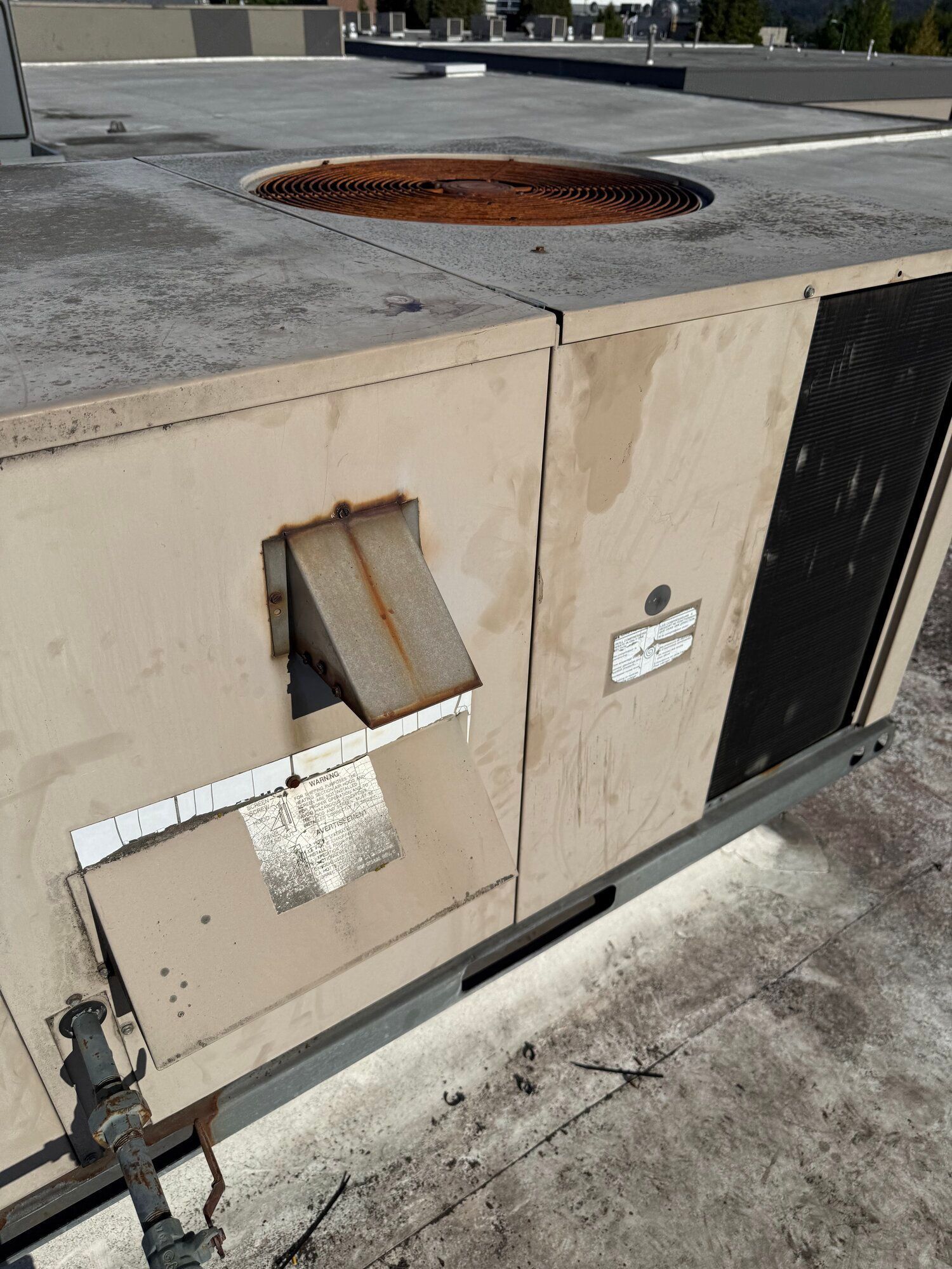 Exterior view of a beige rooftop HVAC unit with a rusted vent and visible labels on a flat roof.