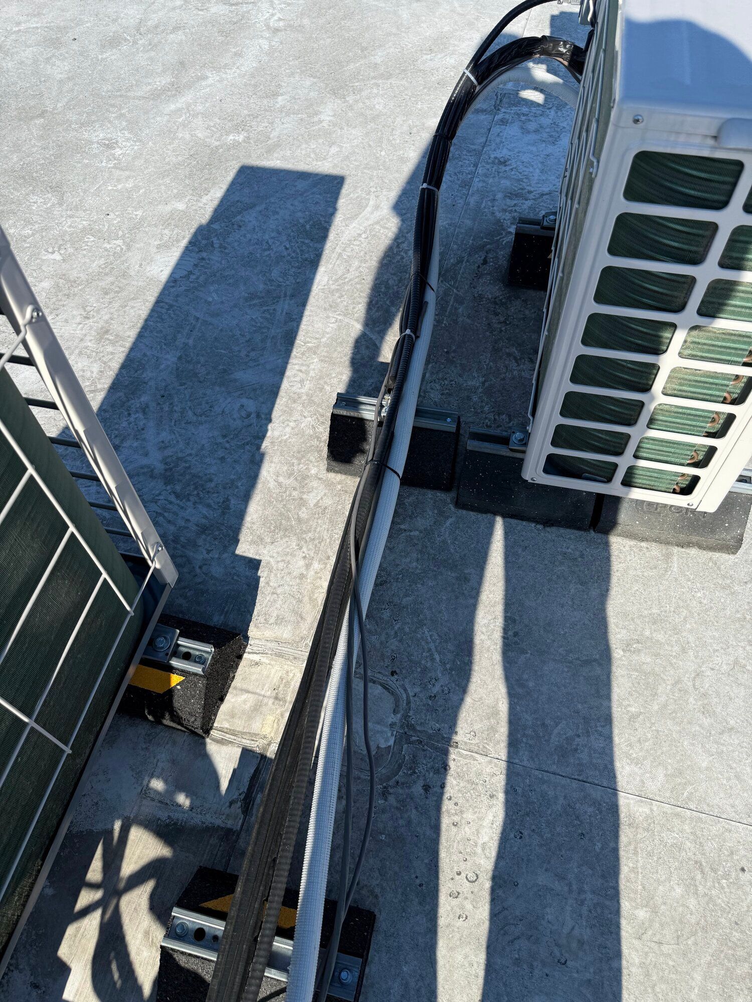 Solar panels and air conditioner units on a rooftop, casting long shadows in daylight.