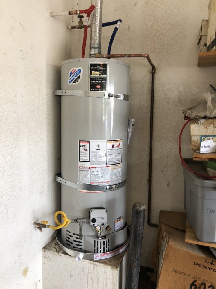 A tall, gray water heater in a corner. Red and blue pipes connect to it. A yellow gas line is visible.