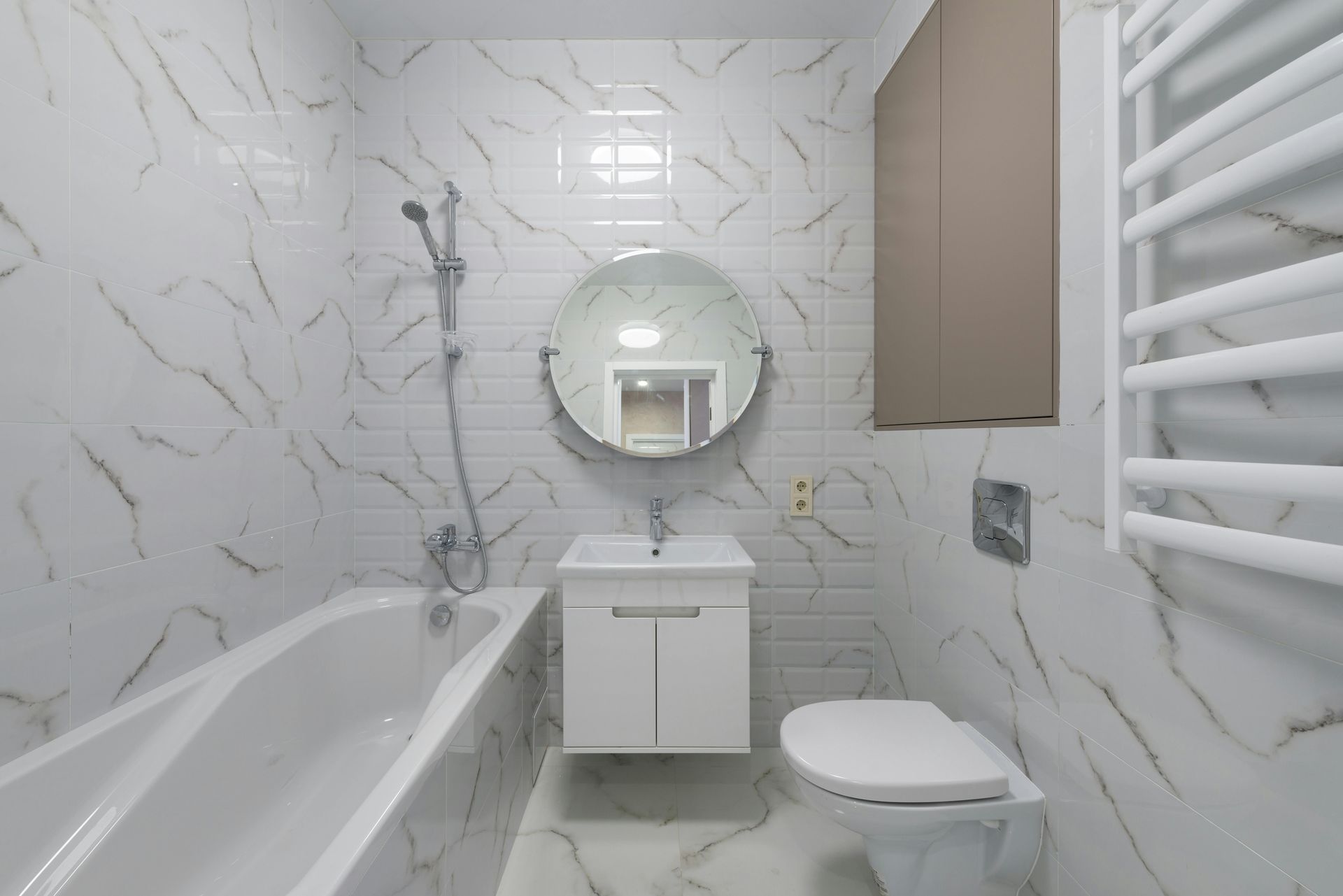 Modern bathroom with white marble-look tile, a tub, toilet, sink, and round mirror.