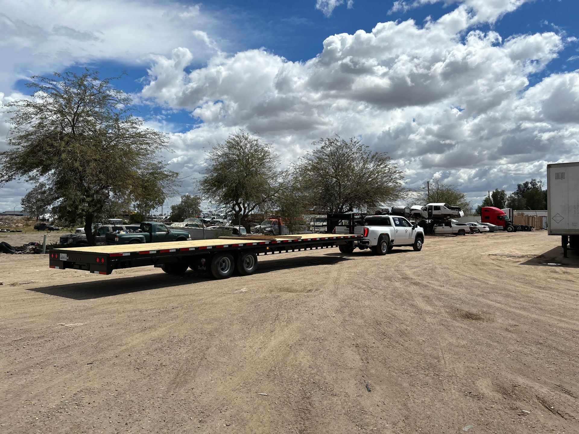 A truck is towing a flatbed trailer in a dirt lot.