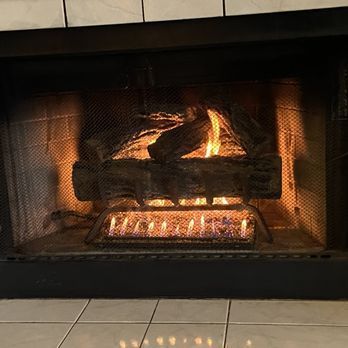 Fireplace with burning gas flames and decorative logs behind a mesh screen.
