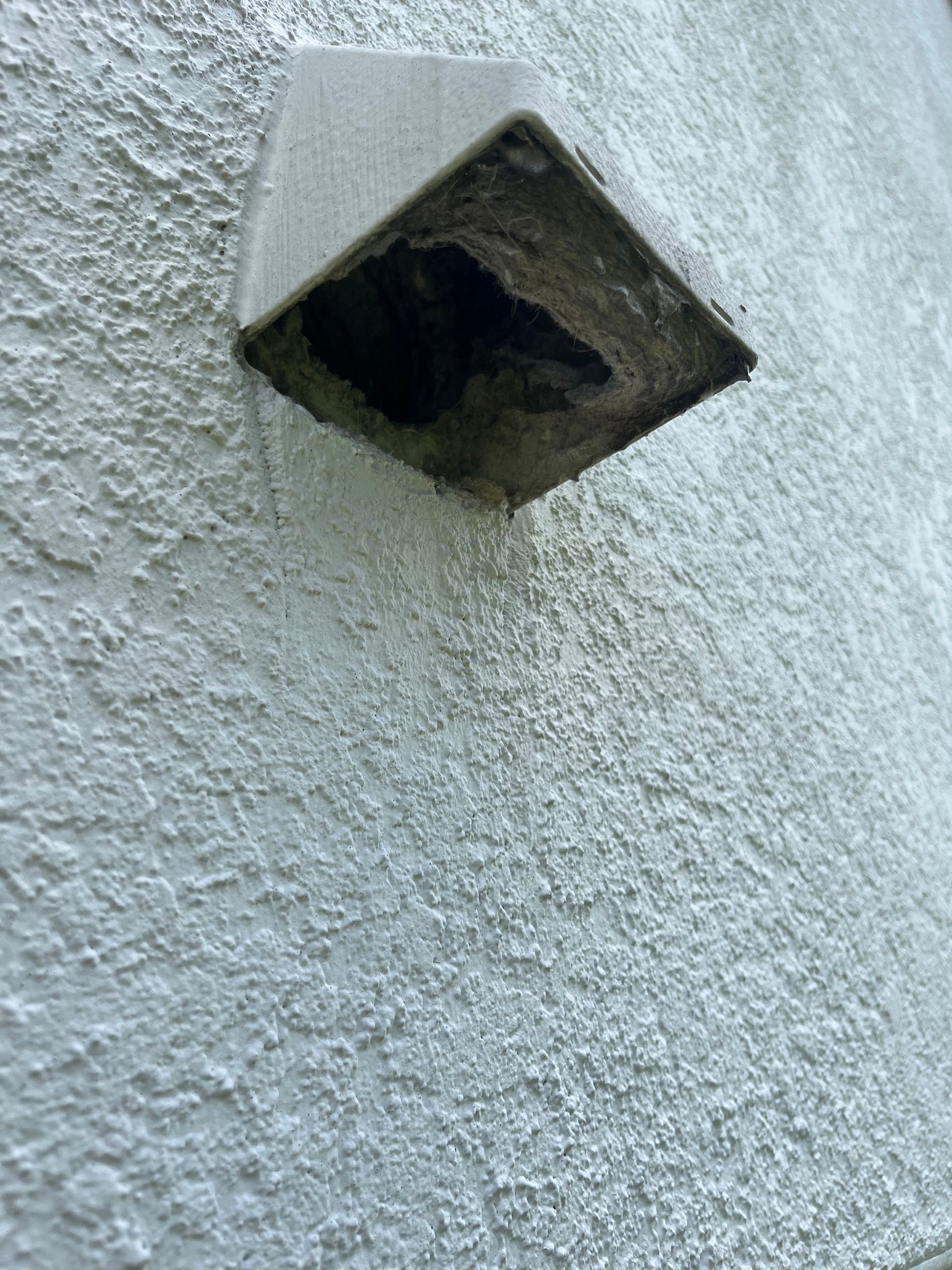 White stucco wall with a gray, square vent dripping water.