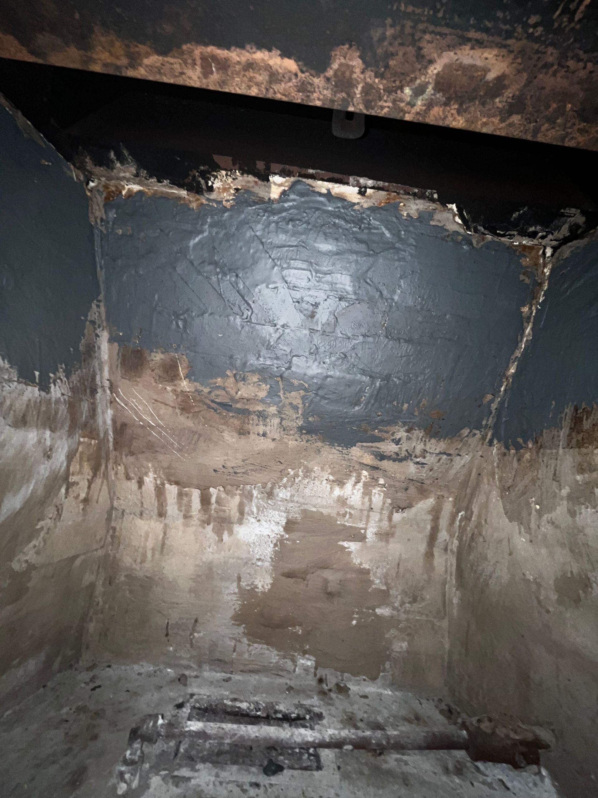 Interior view of a rectangular structure. Dark painted top section with peeling areas, transitioning to lighter walls below.