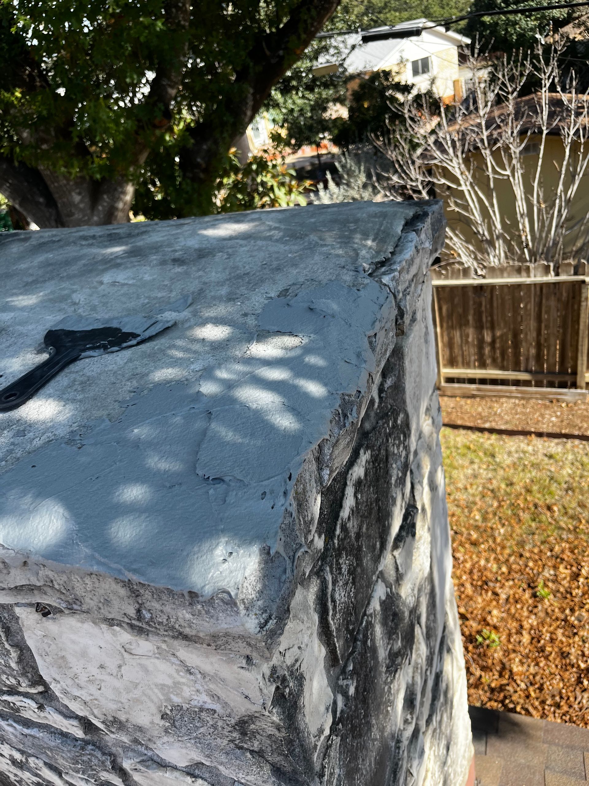 Close-up of a concrete structure with a black marking, sunlight creating shadows. A house and trees are in the background.