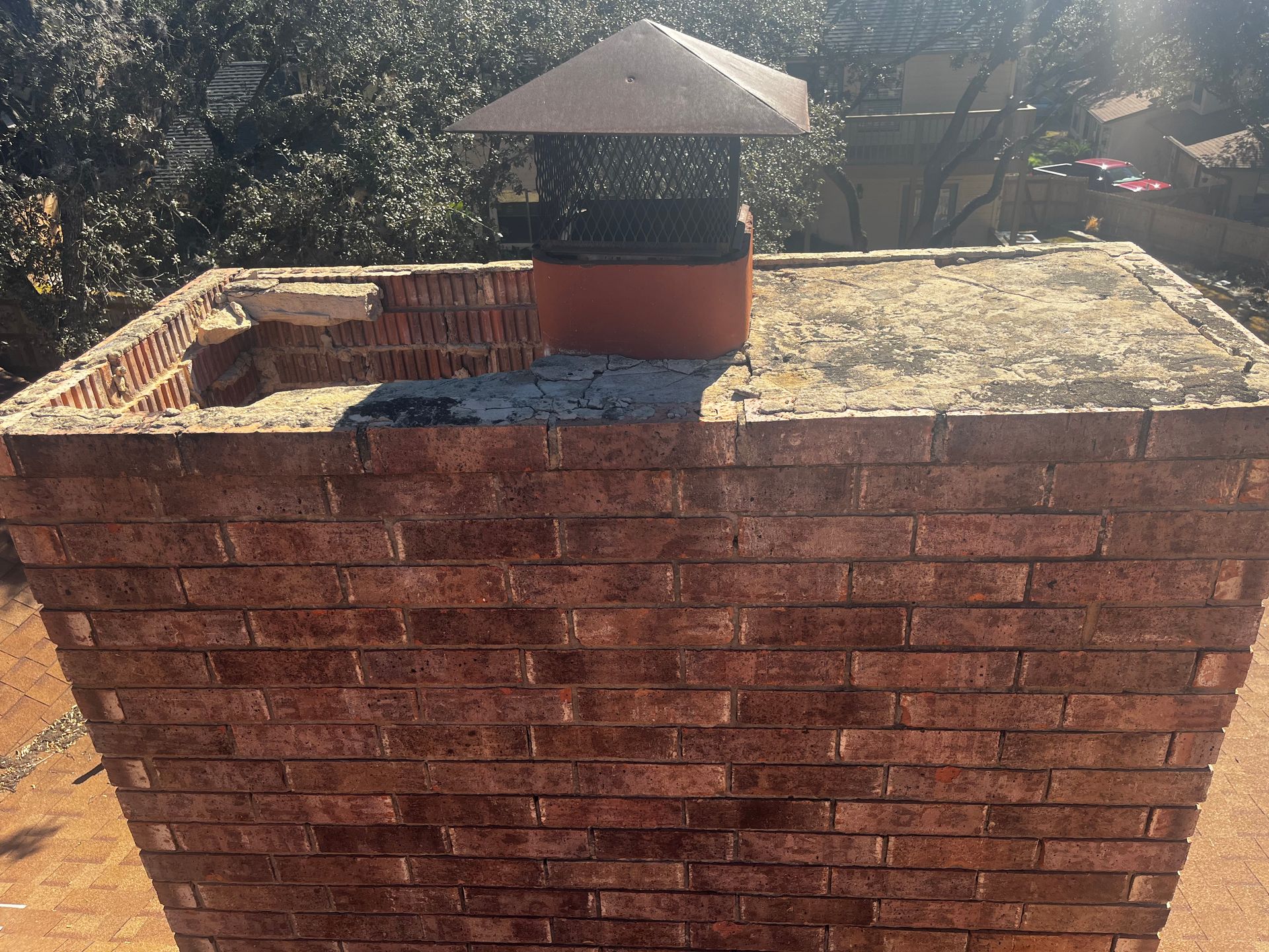 Brick chimney with a metal cap on a rooftop.