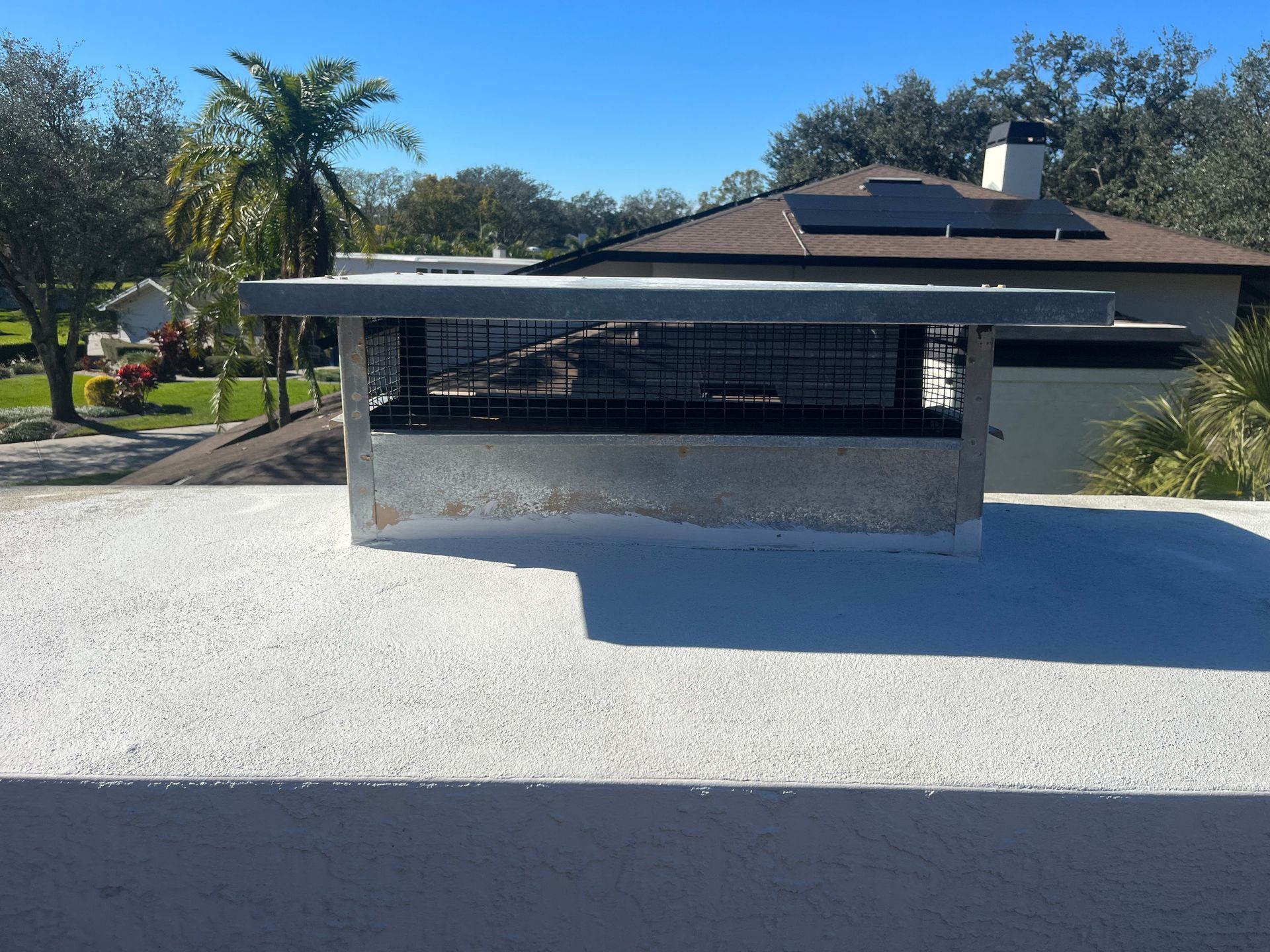 Outdoor structure with concrete base and metal roof, against a house on a sunny day.