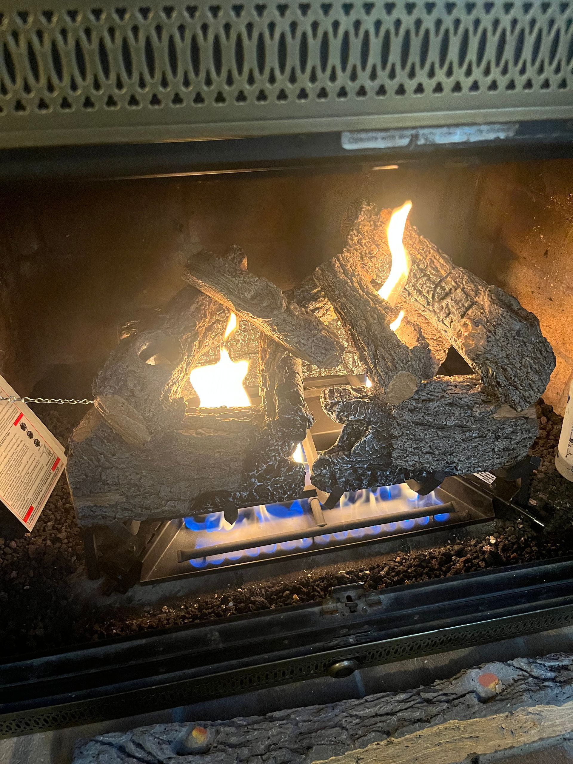 Gas fireplace with burning artificial logs, blue flames, and decorative grate.
