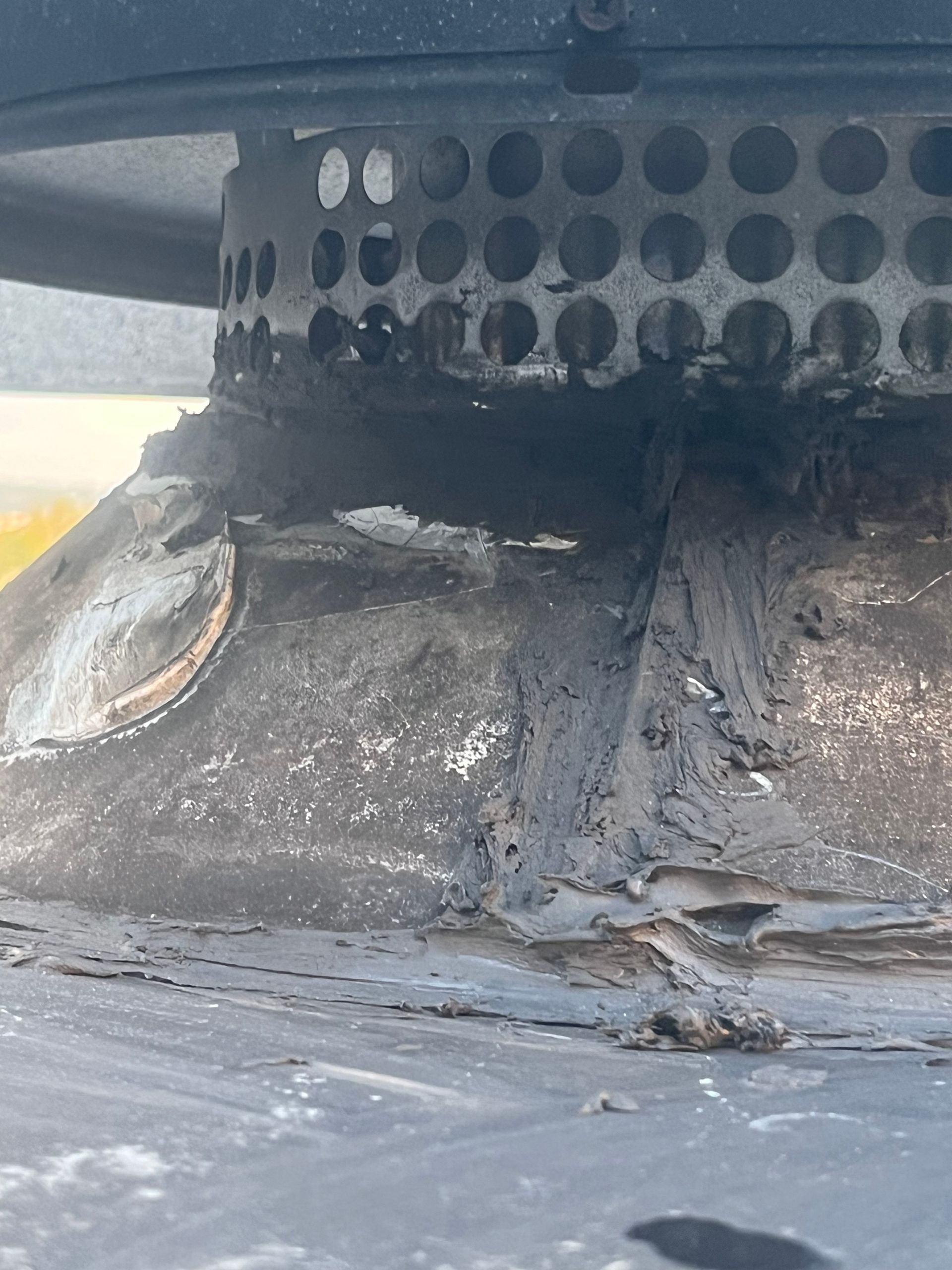 Close-up of a damaged chimney cap and flashing with soot and what appears to be tar-like sealant.