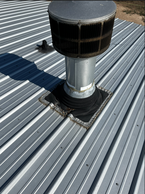 Metal roof with vent pipe; black collar; gray, ridged panels.